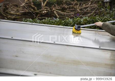 Washing the patio pergola roof cover made of aluminum. removing the dirty algae with brush soap and water close up in garden from a house terrace 99943926