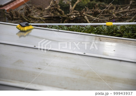 Washing the patio pergola roof cover made of aluminum. removing the dirty algae with brush soap and water close up in garden from a house terrace 99943937