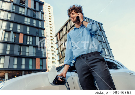 Progressive businessman talking on the phone with recharging electric vehicle. Progressive businessman talking on the phone with recharging electric vehicle. 99946362