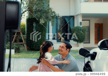 Progressive concept of father and daughter with EV car and home charging station 99946499