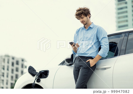 Progressive businessman talking on the phone with recharging electric vehicle. Progressive businessman talking on the phone with recharging electric vehicle. 99947082