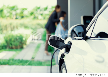 Focus progressive EV car at home with blur woman in background. 99947167