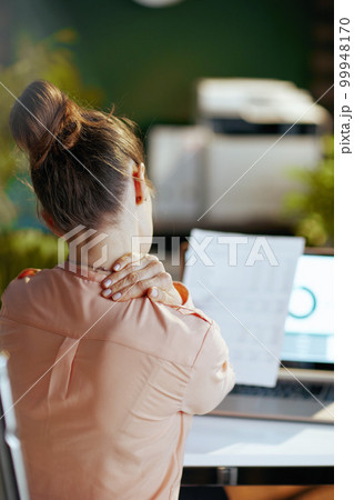 Seen from behind modern business woman having neck pain Seen from behind modern business woman having neck pain 99948170