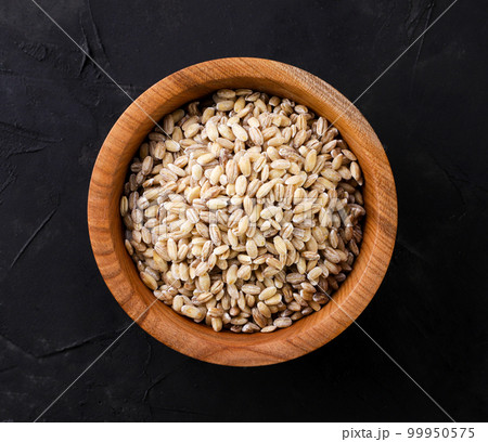 Pearl barley in a wooden plate on a dark background. top view 99950575