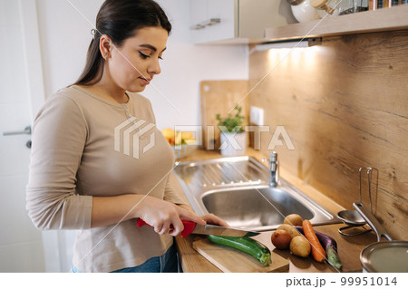 Beautiful young female cutting vegetables on kitchen at home. Home food concept Beautiful young female cutting vegetables on kitchen at home. Home food concept 99951014