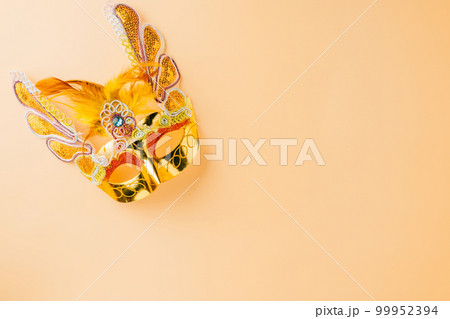 Happy Purim carnival decoration. Golden venetian ball mask isolated on pastel background, Jewish Purim and Mardi Gras in Hebrew, holiday background banner design with copy space, Masquerade party 99952394