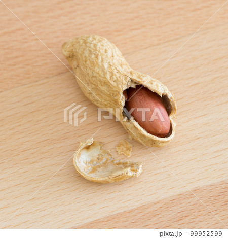 Half peeled peanut with cracked shell on a wooden table. 99952599