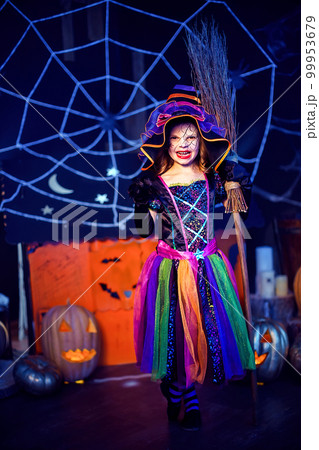 Full length of little girl in witch costume scaring, making faces with broom. Halloween party 99953679