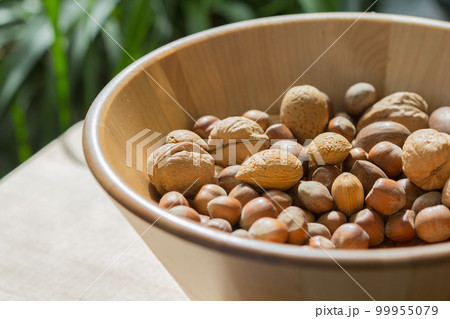 Assorted various nuts in a big wooden bowl against a leafy green background Assorted various nuts in a big wooden bowl against a leafy green background 99955079