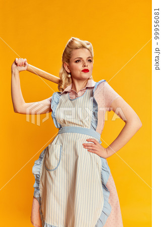 Housekeeper, lady. Portrait of beautiful young blonde woman with stylish hairstyle posing against yellow studio background. Concept of beauty and pin-up style Housekeeper, lady. Portrait of beautiful young blonde woman with stylish hairstyle posing against yellow studio background. Concept of beauty and pin-up style 99956081