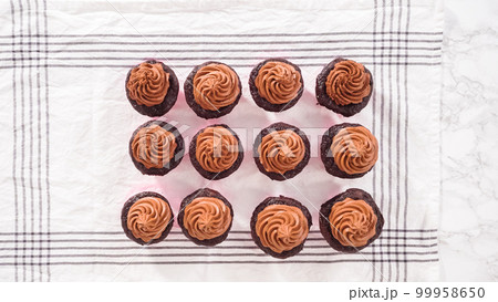 Flat lay. Step by step. Piping chocolate ganache frosting on top of chocolate cupcakes. 99958650