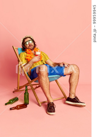 Tired beachgoer. Man in summer shirt and short with Hawaiian flower garland on chest sleeping on sun lounger over pink background. Vacation, summer, rest and male hobbies concept 99959945