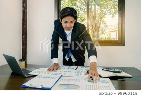 Businessman holding pen, analysis the graph with laptop at the home office 99960118