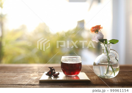Rosella Juice in a glass cup on wooden tray and rose flower in a glass vase 99961154