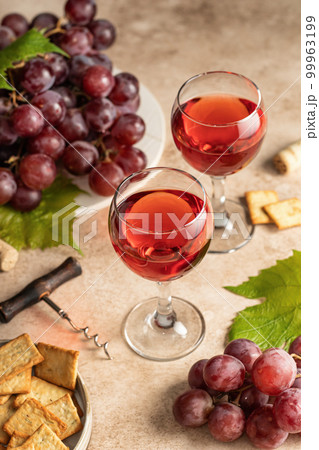 Two glasses of red wine, a bunch of red grapes, crackers and corkscrew on beige textured background. Celebration party for two concept 99963199