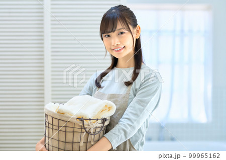 バスルームで洗濯物を運ぶエプロンを着た笑顔の若い主婦 バスルームで洗濯物を運ぶエプロンを着た笑顔の若い主婦 99965162