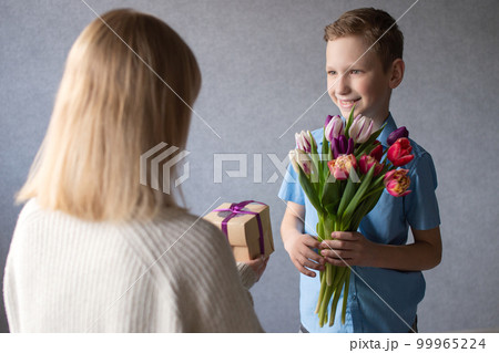 Cute boy gives a bouquet of tulips and a box with a gift to mom Cute boy gives a bouquet of tulips and a box with a gift to mom 99965224
