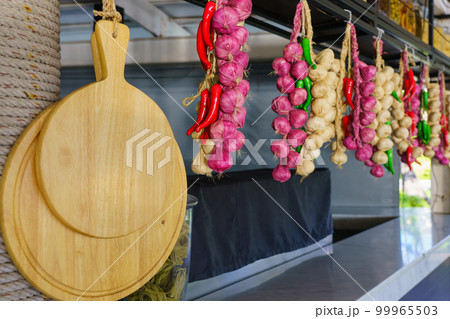 Garlic, onion and chilli, autumn season product, hanging on wooden logs in kitchen 99965503