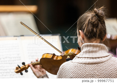 Professional symphonic string orchestra performing on stage and playing a classical music concert, violinist in a foreground 99967751