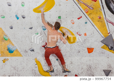 Young climber climbing on the boulder wall indoor, rear view, concept of extreme sports and bouldering Young climber climbing on the boulder wall indoor, rear view, concept of extreme sports and bouldering 99967754