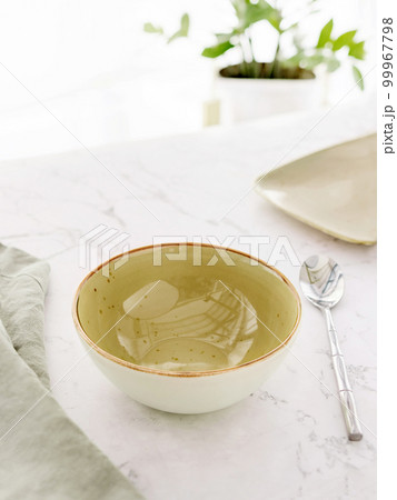Empty green soup bowl with tablecloth and spoon on white marble table 99967798