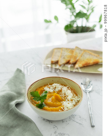 Bowl of pumpkin or carrot vegetarian cream soup decorated by fresh parsley and grated cheese white marble table Bowl of pumpkin or carrot vegetarian cream soup decorated by fresh parsley and grated cheese white marble table 99967818