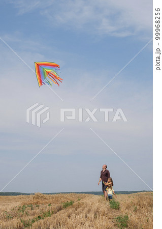 The father and the girls are flying a kite in a mown wheat field. Kids have fun spending the weekend with Dad. The father and the girls are flying a kite in a mown wheat field. Kids have fun spending the weekend with Dad. 99968256
