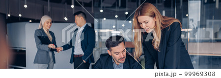 Two smiling coworkers working together analyzing the charts in office on colleagues background Two smiling coworkers working together analyzing the charts in office on colleagues background 99969308