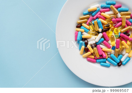 Colorful pills in a large white bowl on a blue background. The concept of health and evidence-based medicine. 99969507