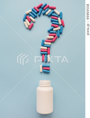 A question mark consisting of three multi-colored vitamins on a blue background along with a plastic white vial. Health problems and treatment. The concept of evidence-based medicine. 99969508