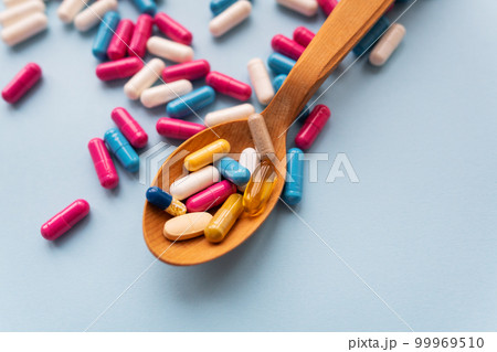 Various bright pills on a blue background lie in a wooden spoon against the background of different bright pills. Health care concept, close-up. 99969510
