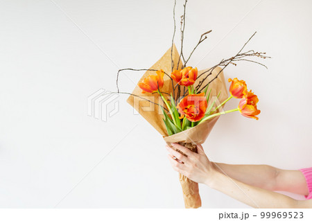 The girl holds in her hands a very beautiful spring bouquet of orange peony tulips along with branches of young cherries. The girl holds in her hands a very beautiful spring bouquet of orange peony tulips along with branches of young cherries. 99969523