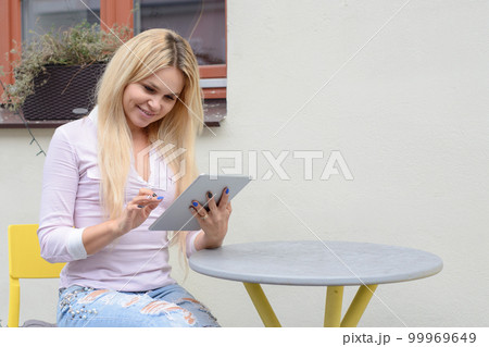 blond girl sitting at a table near a cafe, looking for something 99969649