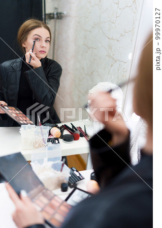 Reflection on a mirror of a woman applying eye shadow 99970127
