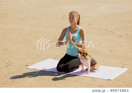 woman and dog meditate on yoga mat on ocean in morning. sports outdoor for mental health woman and dog meditate on yoga mat on ocean in morning. sports outdoor for mental health 99973863