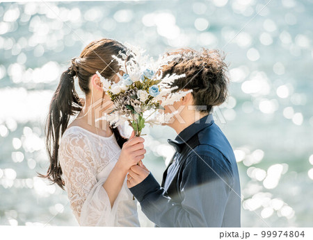 ブーケを持ち顔を見合わせる新郎新婦 99974804
