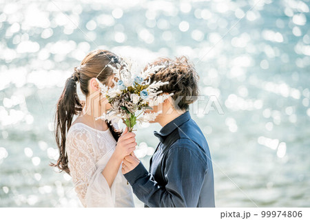 ブーケを持ち顔を見合わせる新郎新婦 99974806
