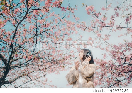 桜バックに音楽を聴く女性の写真 99975286