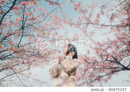 桜バックに音楽を聴く女性の写真 桜バックに音楽を聴く女性の写真 99975287