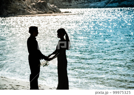海辺で顔を見合わせる新郎新婦 99975325