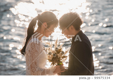 海辺で顔を見合わせる新郎新婦 99975334