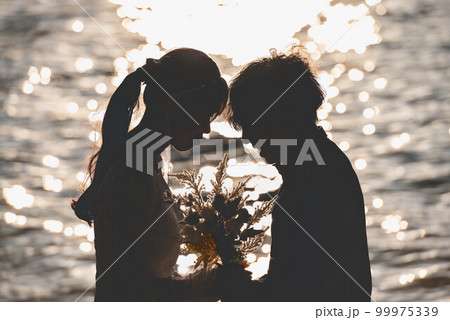 海辺で顔を見合わせる新郎新婦 99975339