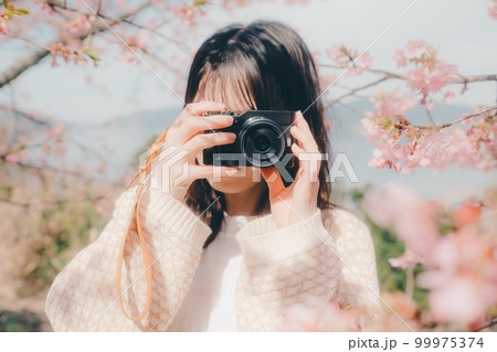 桜バックにミラーレスカメラを持っている女性の写真 桜バックにミラーレスカメラを持っている女性の写真 99975374