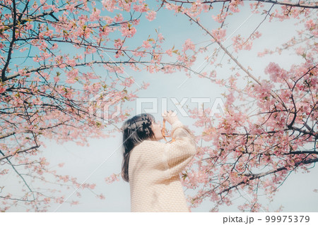 桜バックにミラーレスカメラを持っている女性の写真 桜バックにミラーレスカメラを持っている女性の写真 99975379