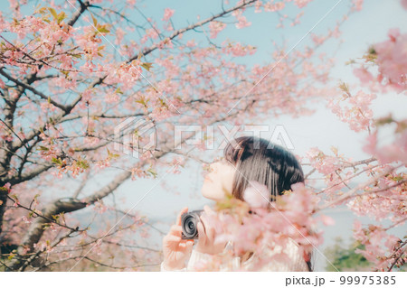 桜バックにミラーレスカメラを持っている女性の写真 桜バックにミラーレスカメラを持っている女性の写真 99975385