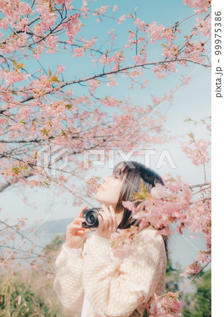 桜バックにミラーレスカメラを持っている女性の写真 99975386