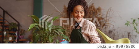 Smiling woman florist taking care of plant watering it in floral shop 99976880