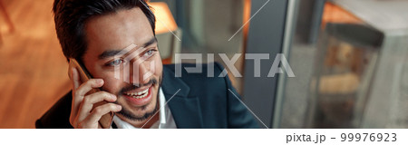 Happy indian businessman is talking phone with client during lunch time in cozy cafe Happy indian businessman is talking phone with client during lunch time in cozy cafe 99976923