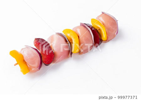 Raw chicken leg meat skewers with vegetables,plums,peppers,onions, on a white background.Uncooked mixed meat skewer with peppers.Skewers with pieces of raw meat, red, yellow and green pepper.Top view. 99977371