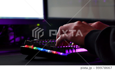 Male hands is typing on the computer keyboard, close up view. Man working on the pc computer. Human hands typing on the colourful gaming keyboard. Fingers typing on the led rgb keyboard. 99978667